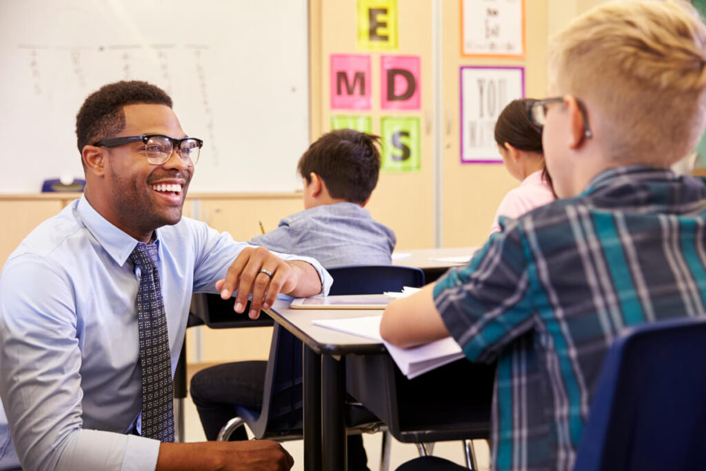 image of a teacher down on one kneel and smiling while communicating with his pupil