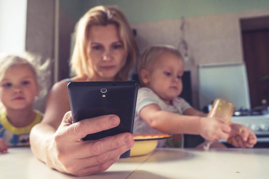 image of a woman working on her phone surrounded by her 2 children
