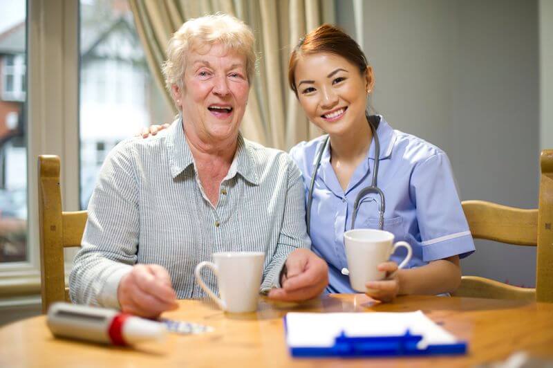 Image of a healthcare assistant and her elderly client drinking coffee