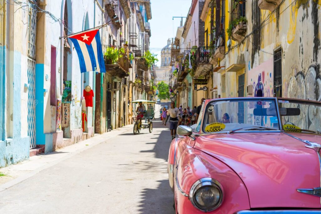 A street in Havana, Cuba with a pink classic car parked on the street.