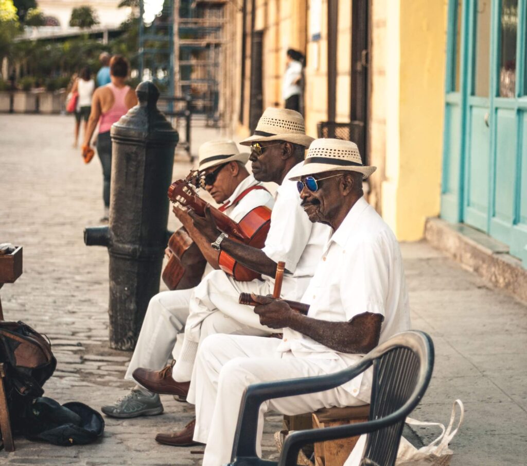 3 elderly black men wearing white clothes and playing musical instruments in Havana, Cuba