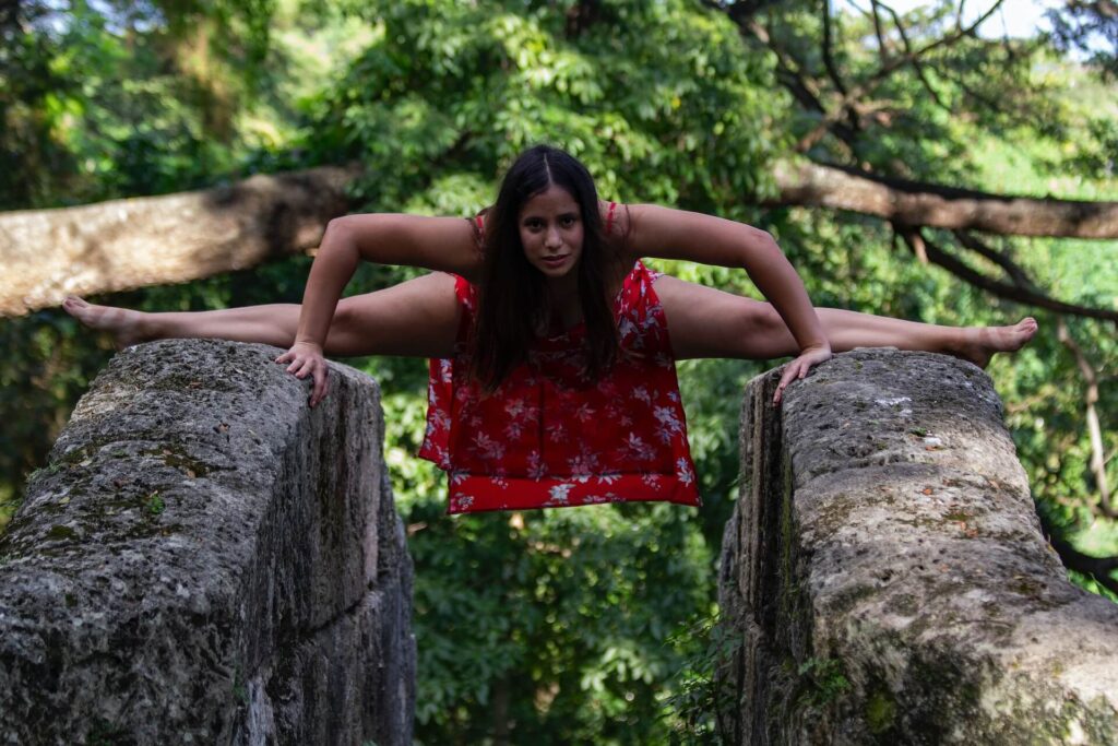 A local in Cuba wearing a red dress and stretching on 2 fences.