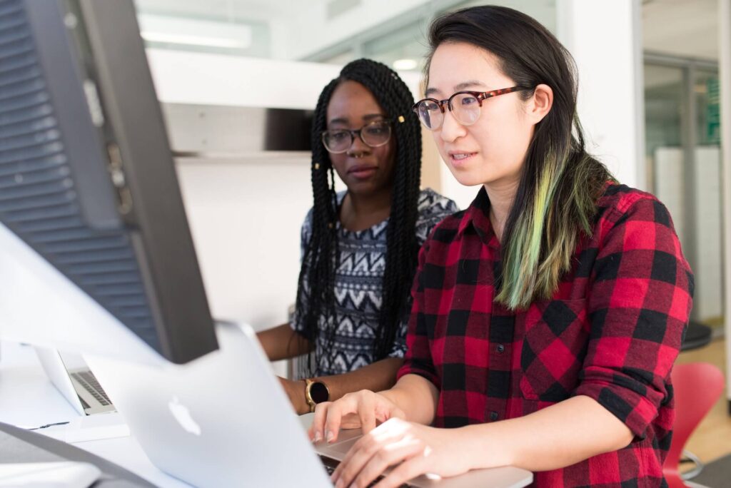 1 Asian woman and 1 black woman working on the same computer, both of whom are interns at Intesa Sanpaolo