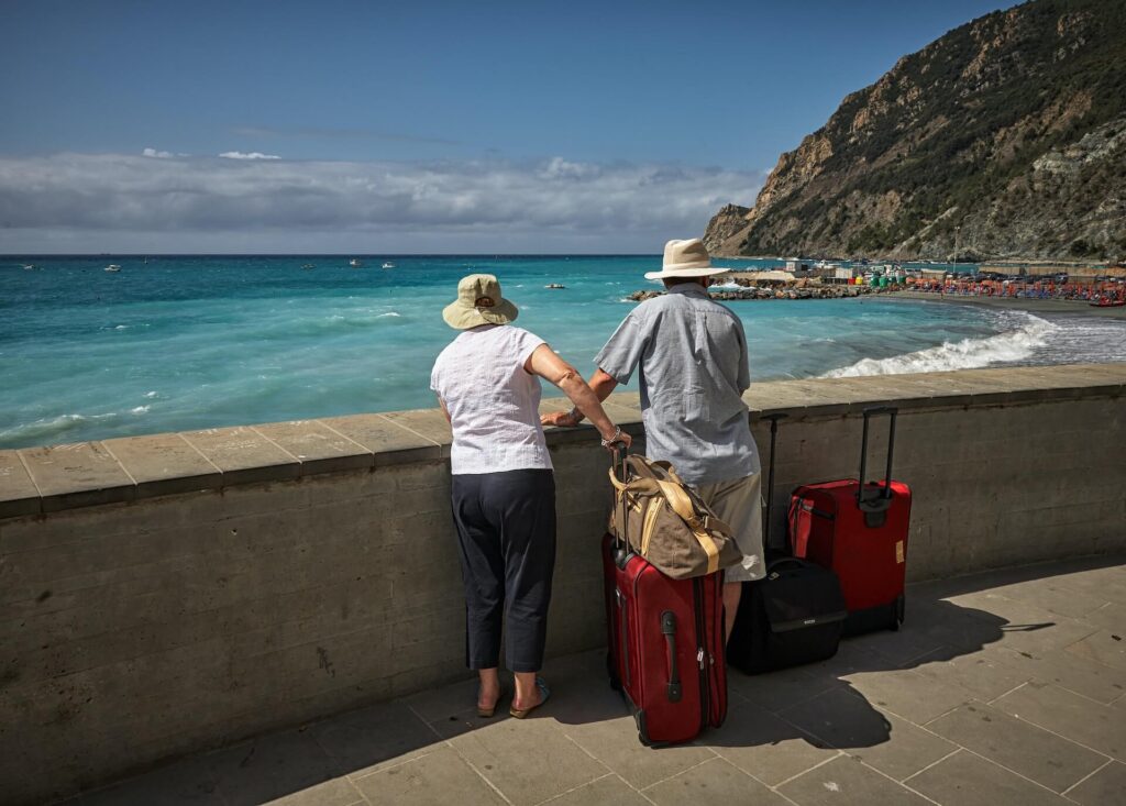 A couple standing by the beach with their luggage and travel pass