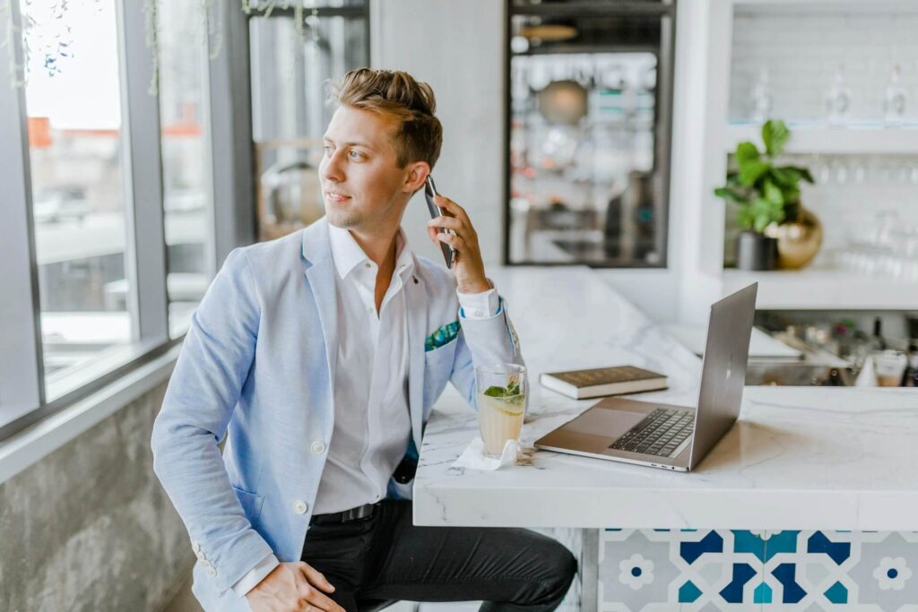 A man sitting down in front of a computer talking to someone over the phone about how to become a travel agent